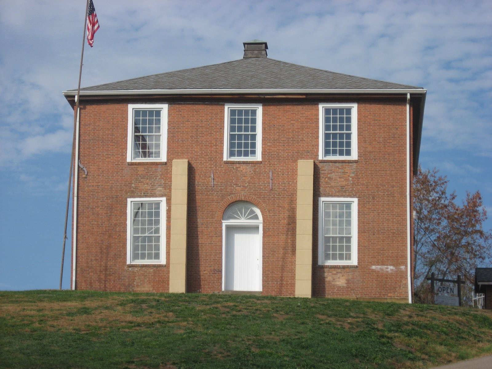 The old Meigs County Courthouse at Chester, Ohio — a two-storey red brick building with white-trimmed windows, standing on a grassy rise beside the United States flag.